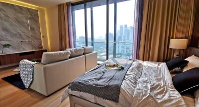 Modern bedroom with a city view, featuring a bed, a sofa, and large windows.