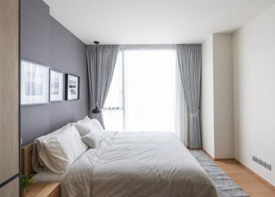 A modern bedroom with a double bed, gray accent wall, and large window with curtains