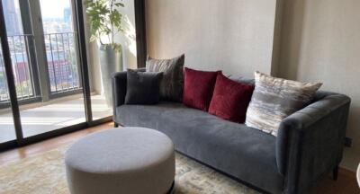 Living room with a gray sofa, round ottoman, and large windows