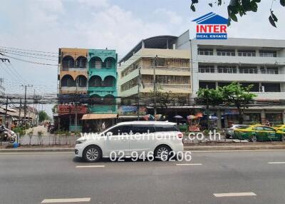 Street view of buildings with vehicles on road and real estate sign