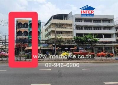 Exterior shot of multiple buildings along a main road with visible traffic and a real estate sign