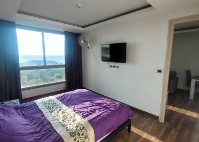 Bedroom with bed, wall-mounted TV, wooden flooring, and large window with curtains