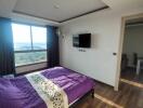 Bedroom with bed, wall-mounted TV, wooden flooring, and large window with curtains