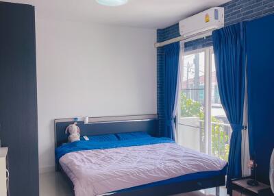 A modern bedroom with blue and white decor, featuring a bed with blue bedding, nightstands, a lamp, and a window with blue curtains.