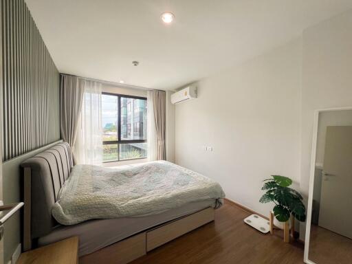 Spacious bedroom with large window, bed, air conditioner, and wooden flooring