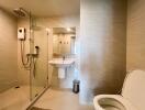 Modern bathroom with glass shower enclosure, wall-mounted sink, and toilet