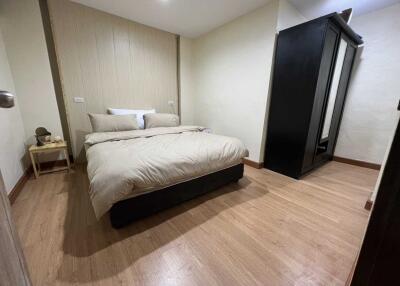 A cozy bedroom with wooden flooring, a neatly made bed, a small bedside table, and a wardrobe
