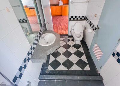 Bathroom with checkered tile flooring, toilet, sink, and view into an adjacent room