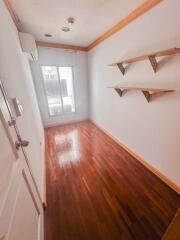 Empty room with wooden floors, two wall-mounted shelves, an air conditioning unit, and a glass door leading outside.