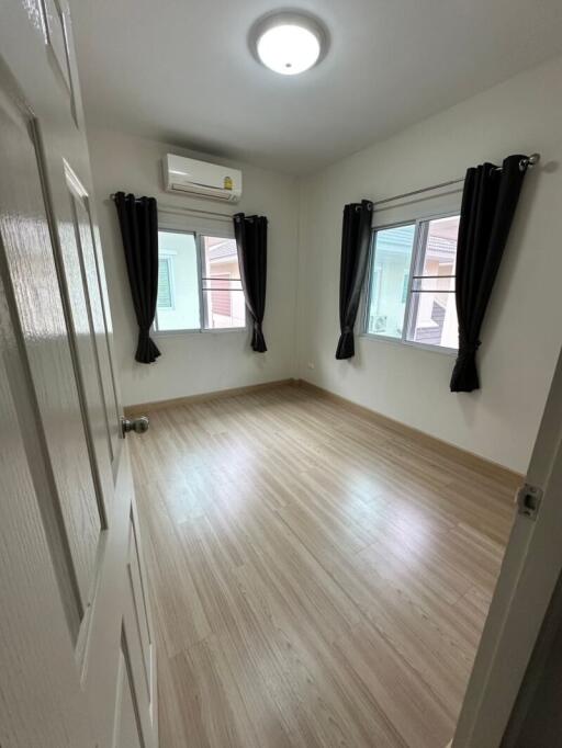 Empty bedroom with wooden floor, curtains, and air conditioning