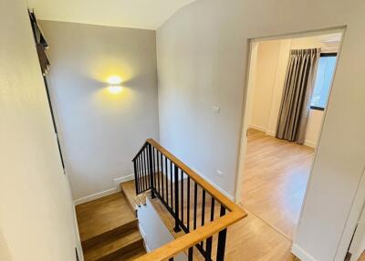 Well-lit staircase with wooden steps and metal railings leading to an upper floor with a view into a room