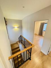 Well-lit staircase with wooden steps and metal railings leading to an upper floor with a view into a room