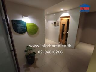 Hallway with a wooden door, a potted plant, information signs, and lighting