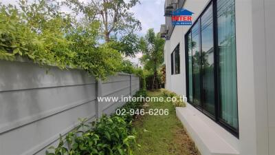 A well-maintained side yard with a white fence and green foliage alongside a white building