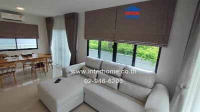 Modern living room with large windows, white sofa, and dining area in view