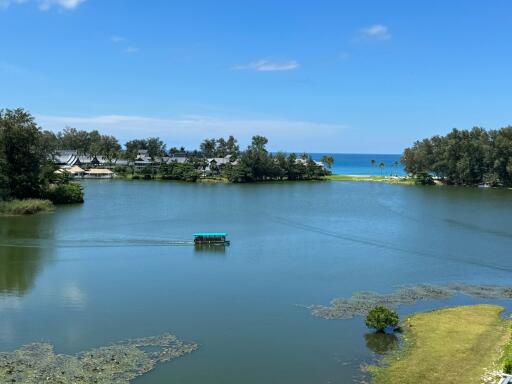 View of tranquil lake with a boat, surrounded by greenery and a distant seashore