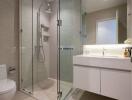 Modern bathroom with glass shower, white vanity, and toilet