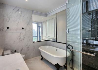 Modern bathroom with white marble walls, freestanding bathtub, glass-enclosed shower, and wide vanity mirror