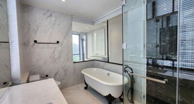 Modern bathroom with white marble walls, freestanding bathtub, glass-enclosed shower, and wide vanity mirror