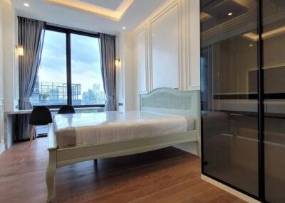 Modern bedroom with a large window offering a city view, wooden floors, a bed, and a workspace