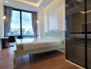 Modern bedroom with a large window offering a city view, wooden floors, a bed, and a workspace