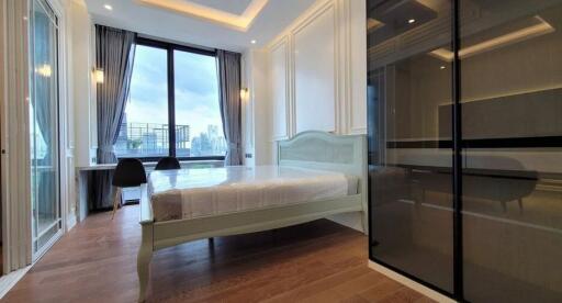 Modern bedroom with a large window offering a city view, wooden floors, a bed, and a workspace