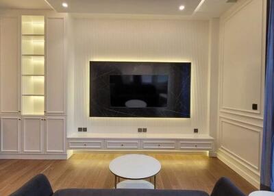 Modern living room with large television, built-in shelves, and hardwood floors