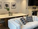 Modern living room with a dining area, including a grey sofa, white marble dining table, wall art, and an open kitchen in the background