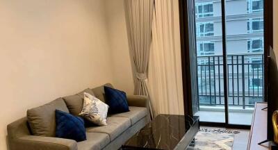 Modern living room with a gray sofa, blue accent pillows, marble coffee table, large window with city view and balcony access