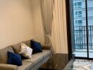 Modern living room with a gray sofa, blue accent pillows, marble coffee table, large window with city view and balcony access