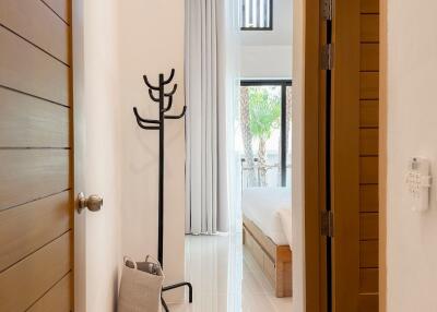 A hallway leading to a well-lit modern bedroom, featuring tall windows and a minimalist design.