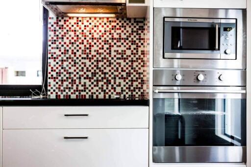 Modern kitchen with mosaic backsplash, oven, microwave, and black countertop
