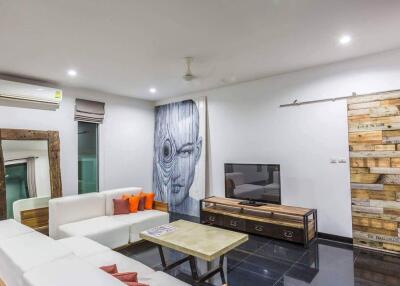 Modern living room with white sectional sofa, wooden coffee table, wall-mounted TV, air conditioner, and unique wooden wall artwork