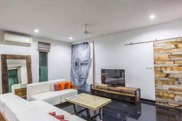 Modern living room with white sectional sofa, wooden coffee table, wall-mounted TV, air conditioner, and unique wooden wall artwork