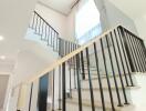 Modern staircase in a well-lit area with black railing and large window