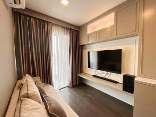 Modern living room with large TV, sofa, and floor-to-ceiling windows with curtains