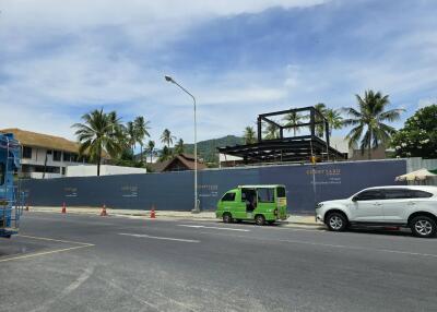 Street view of a construction site with palm trees and mountains in the background