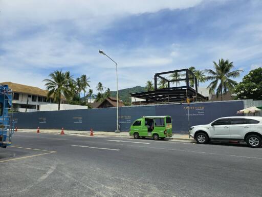 Street view of a construction site with palm trees and mountains in the background