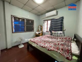 Bedroom with a double bed, wooden floor, air conditioner, windows with curtains, fan, and a small dressing table with a mirror