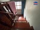 Staircase with wooden handrail and steps, leading to a window with curtains