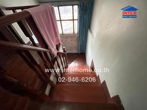 Staircase with wooden handrail and steps, leading to a window with curtains