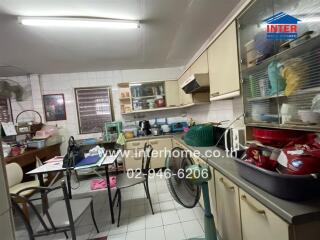 Messy kitchen with cluttered countertops and a dining table with items on it.