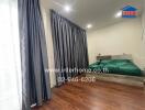 Bedroom with wooden flooring, green bedspread, and large window with gray curtains