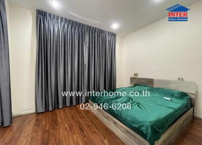 Spacious bedroom with wooden flooring and large windows covered with dark curtains.