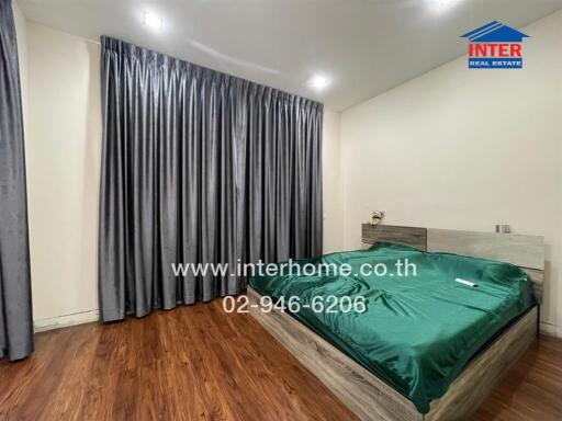 Spacious bedroom with wooden flooring and large windows covered with dark curtains.