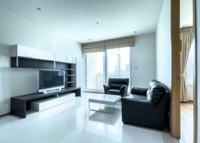 Modern living room with white floor tiles, black leather furniture, TV, wall shelves, and large windows with city view.