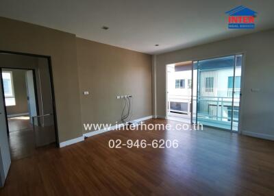 Spacious living room with wooden flooring, large windows, and balcony access.