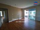 Spacious living room with wooden flooring, large windows, and balcony access.