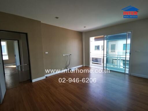 Spacious living room with wooden flooring, large windows, and balcony access.