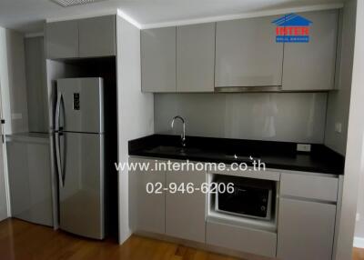 Modern kitchen with grey cabinets, stainless steel refrigerator, built-in microwave and black countertop